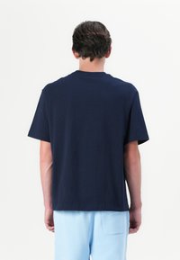 T-shirt en coton bleu marine avec des manches courtes, un col rond et une coupe décontractée. Porté avec un short bleu clair, mettant en valeur un design simple.