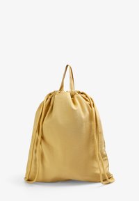Mochila tipo saco de tela amarilla suave, con parte superior recogida y un solo asa, con superficie texturizada y cierres de cordón.