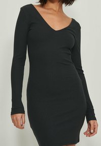 Robe tricotée noire à côtes avec des manches longues et un décolleté en V profond, silhouette ajustée, texture lisse, coupe mi-genoux.