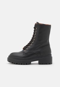 Černá kožená šněrovací bota s texturovaným povrchem, zlatými očky, robustní podrážkou a prošívaným vzorem. Boční zip pro snadné obutí a vyjímatelná stélka.