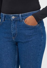 Μπλε τζιν παντελόνι με μέτρια πλύση, διαθέτοντας μπροστινή τσέπη, αντίθετο ραφί και κλείσιμο με κουμπί στη μέση.