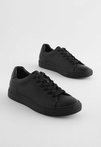 Svarta sneakers med överdel i texturerat läder, snörningsdesign, rund tå och gummisula. Har minimalistiska detaljer på sidorna.