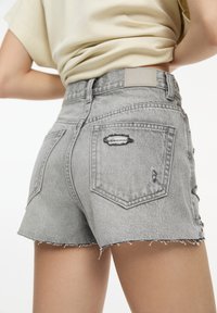 Sivé denim šortky s rozstrapkaným okrajom, poškodenými detailmi a dvoma zadnými vreckami. Majú šitú oblasť pásu s hladkou textúrou.