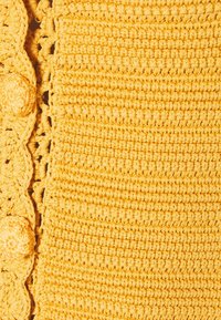 Tissu en crochet jaune avec un design texturé. Des bords festonnés notables et des accents de boutons ronds rehaussent le détail visuel global.