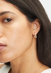 Örhängen i roséguld med en rektangulär design och en slät yta, som visar en modern och minimalistisk estetik.