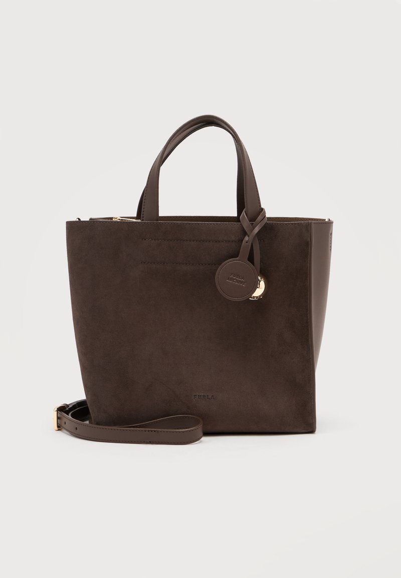Sac fourre-tout en daim brun foncé avec deux poignées, une bandoulière amovible et une étiquette ronde en cuir avec détail doré.