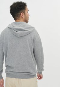 Grå bomullsblandning hoodie med en mysig huva, ribbade mudd och fåll, med en mjuk textur och avslappnad passform, visad bakifrån.