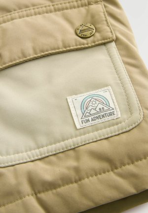 Tissu d'extérieur beige avec un patch cousu mettant en avant un design de montagne et de soleil. Comprend un bouton-pression en laiton et une texture douce.
