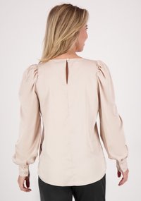 Lichtbeige blouse met puffed mouwen, een sleutelgat uitsnijding op de rug en een knoopsluiting. Glad stof met een strakke, getailleerde pasvorm.