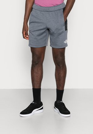 Grå sportshorts med en texturerad yta, elastisk midja, svarta sidopaneler och vit logodetalj. I kombination med svarta sneakers och strumpor.