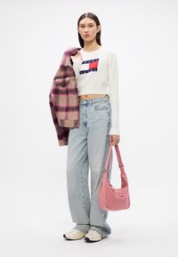 Biely krátky sveter s logom "TOMMY JEANS", svetlomodré nohavice s vysokým pásom, ružová kabelka na rameno a vzorovaný károvaný kabát v odtieňoch béžovej a ružovej.