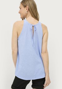 Lichtblauw mouwloos shirt met een textuurafwerking, een keyhole achterkant en een strik. Gecombineerd met zwarte opgerolde shorts.