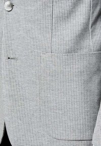 Jasnoszara marynarka w wzór pepitki z dopasowanym guzikiem i zasuwaną kieszenią z klapką po prawej stronie z przodu.