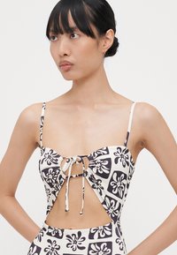 Fekete-fehér virágmintás bikini felsőrész, vékony pántokkal, kivágott középrésszel és elöl megkötő részlettel.