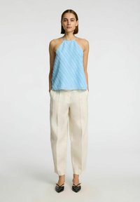 Top halter azzurro chiaro con strisce diagonali strutturate, abbinato a pantaloni a gamba larga color crema e décolleté nere a punta.