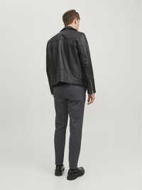 Svart läderjacka med en figurnära design, uppvisad tillsammans med grå avsmalnande byxor och svarta skor. Synliga dragkedjor och en slät yta på jackan.