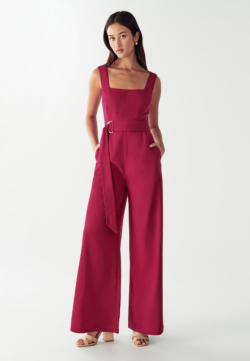 Bordeauxkleurige jumpsuit met een vierkante halslijn, wijde pijpen, een strikceintuur in de taille en zijzakken. Glad materiaal met een strakke silhouet.
