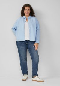 Niebieska i biała koszula w paski zapinana na guziki z długimi rękawami, w połączeniu z niebieskimi dżinsami i białymi trampkami z kremowymi akcentami.