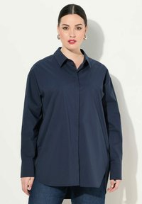 Camisa de botones azul marino de manga larga, con cuello, hecha de tela suave, que presenta un corte relajado y aberturas laterales para mayor comodidad.
