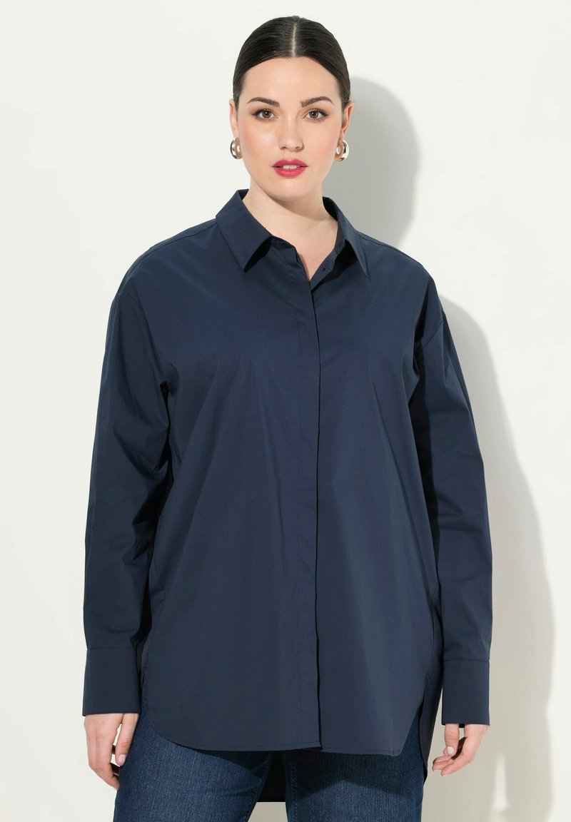 Camisa de botones azul marino de manga larga, con cuello, hecha de tela suave, que presenta un corte relajado y aberturas laterales para mayor comodidad.