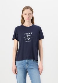 Mørkeblå bomuld T-shirt med korte ærmer, rund halsudskæring, med et hvidt logo print, der inkluderer tekst og etableringsår.