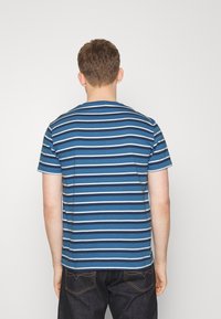 Blå randig t-shirt med varierande nyanser av blått, korta ärmar och rund halsringning. Tyget verkar mjukt med en avslappnad passform.