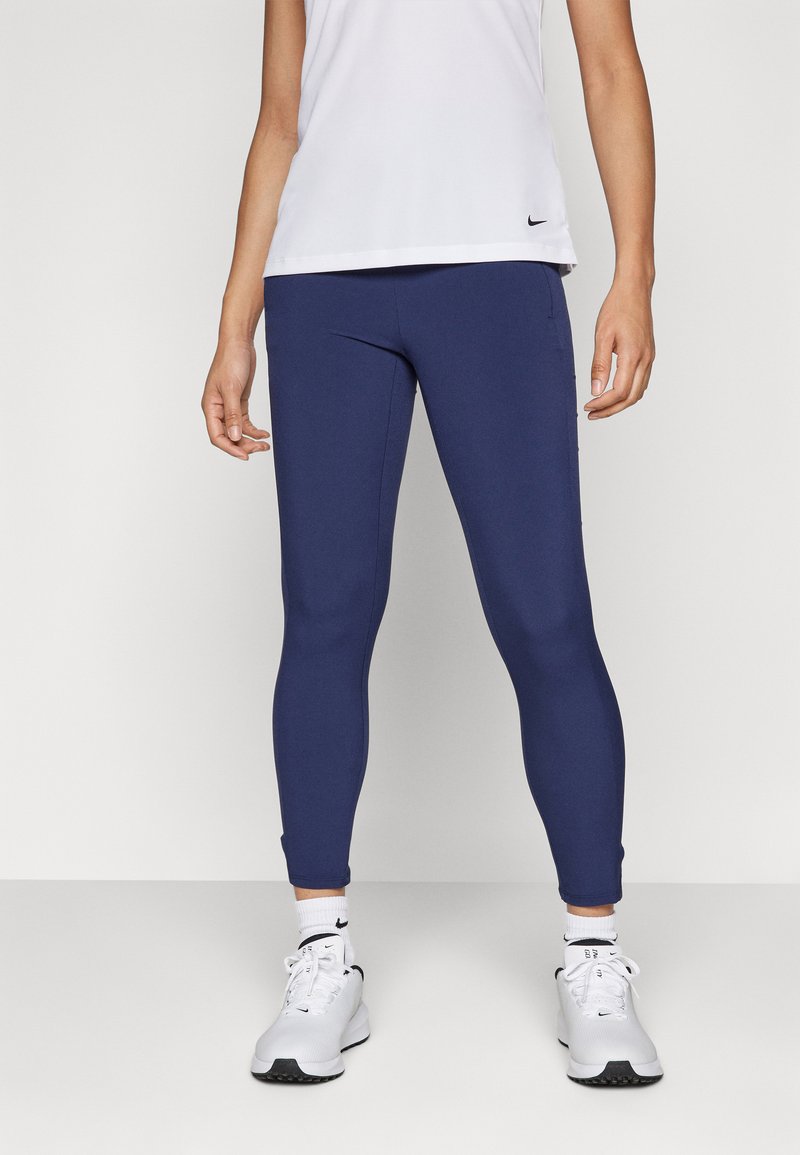 Navy leggings van rekbaar materiaal, met een strakke uitstraling en een aansluitende pasvorm. Gecombineerd met witte sportschoenen en sokken.