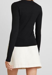 Svart ribbad långärmad topp med en åtsittande design, rundad halsringning och mjuk textur, ihopparad med en ljusfärgad kjol.