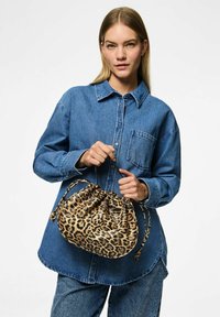 Taška na stažení s leopardím potiskem vyrobená z měkkého materiálu, s kulatým tvarem a splétanými popruhy, kterou drží model v džínové košili.