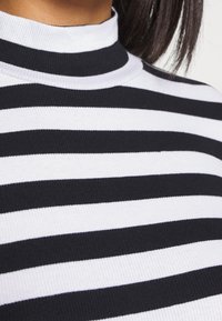 Schwarz-weißer gestreifter Rollkragenpullover aus geripptem Strickstoff. Mit hohem Kragen und abwechselnd breiten und schmalen Streifen.
