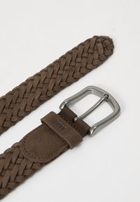 Ceinture en cuir tressé marron avec une boucle en métal argenté. Présente une texture douce et un accent logo sur le rabat en cuir près de la boucle.