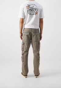 Pantaloni cargo grigio chiaro con molteplici tasche laterali e tasche posteriori a toppa, abbinati a una maglietta bianca con una grafica dettagliata.