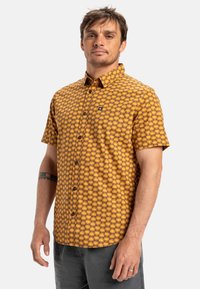 Short-sleeve button-up shirt in yellow with a checkered pattern, featuring a pocket and black logo accent. Cotton material, relaxed fit.