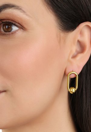 Pendientes de metal en tono dorado con forma ovalada alargada y un acento esférico en la parte inferior. Textura de superficie lisa y acabado pulido.