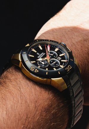 Montre chronographe noire et dorée avec un cadran rond, des marquages des heures luminescents et trois sous-cadrans, montée sur un bracelet texturé noir.