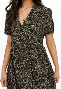 Robe à imprimé léopard noir et beige avec un décolleté en V profond, des manches courtes bouffantes et une jupe à volants. Le tissu semble léger et texturé.