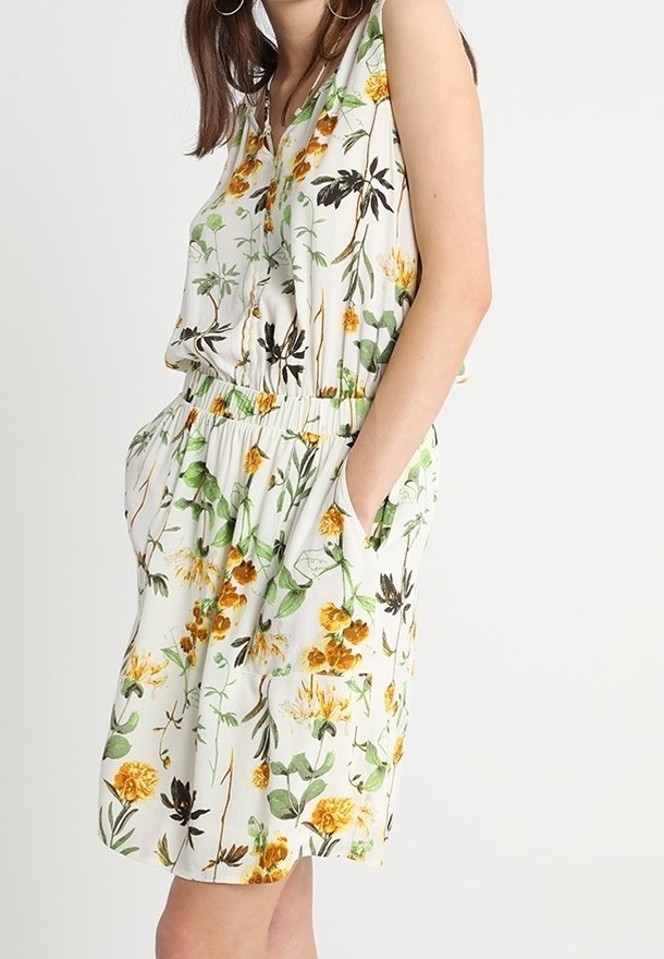 Robe sans manches à motifs floraux sur fond blanc avec des motifs jaunes et verts, taille élastique et poches latérales.