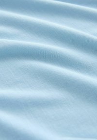 Tissu en coton bleu clair avec une texture lisse, présentant de doux plis et des motifs tissés subtils, créant un flux délicat.