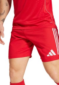 Rote Sportshorts mit vertikal gerippter Textur, weißen adidas-Streifen und einer schlanken Passform. Das Material wirkt leicht und glatt.