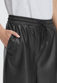 Joggers neri in similpelle con vita elasticizzata, chiusura con coulisse e tasca laterale. Texture liscia e vestibilità comoda.