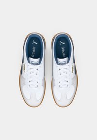 Paire de baskets blanches Puma Palermo avec semelle en gomme, doublure intérieure bleue, lacets blancs et semelles Ortholite, vues de dessus sur fond blanc.