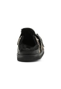Chausson noir en tissu doux avec une surface texturée, comportant un intérieur en peluche et un détail de boucle ajustable sur le côté.