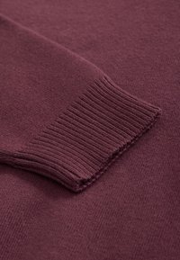 Bordó kötött pulóver ujjának közeli képe, bordás mandzsettával, sima textúrával és puha anyaggal, egységes színárnyalattal.