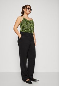 Black wide-leg pants paired with a green zebra-striped tank top. The top features thin straps and a draped design. Black pointed-toe shoes.
