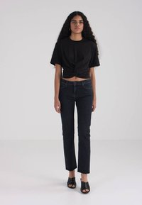 Top corto negro anudado, jeans de talle alto azul oscuro y sandalias de tacón abiertas negras. Tela suave con una silueta ajustada.