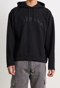 Sudadera con capucha negra de corte holgado, que presenta un logotipo embossado en la parte delantera, cordón en el dobladillo y textura suave.