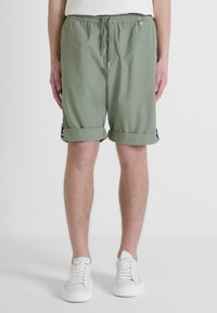 Pantaloni corti verde chiaro realizzati in tessuto morbido, dotati di una vita elasticizzata con coulisse, risvoltini e piccoli dettagli metallici.