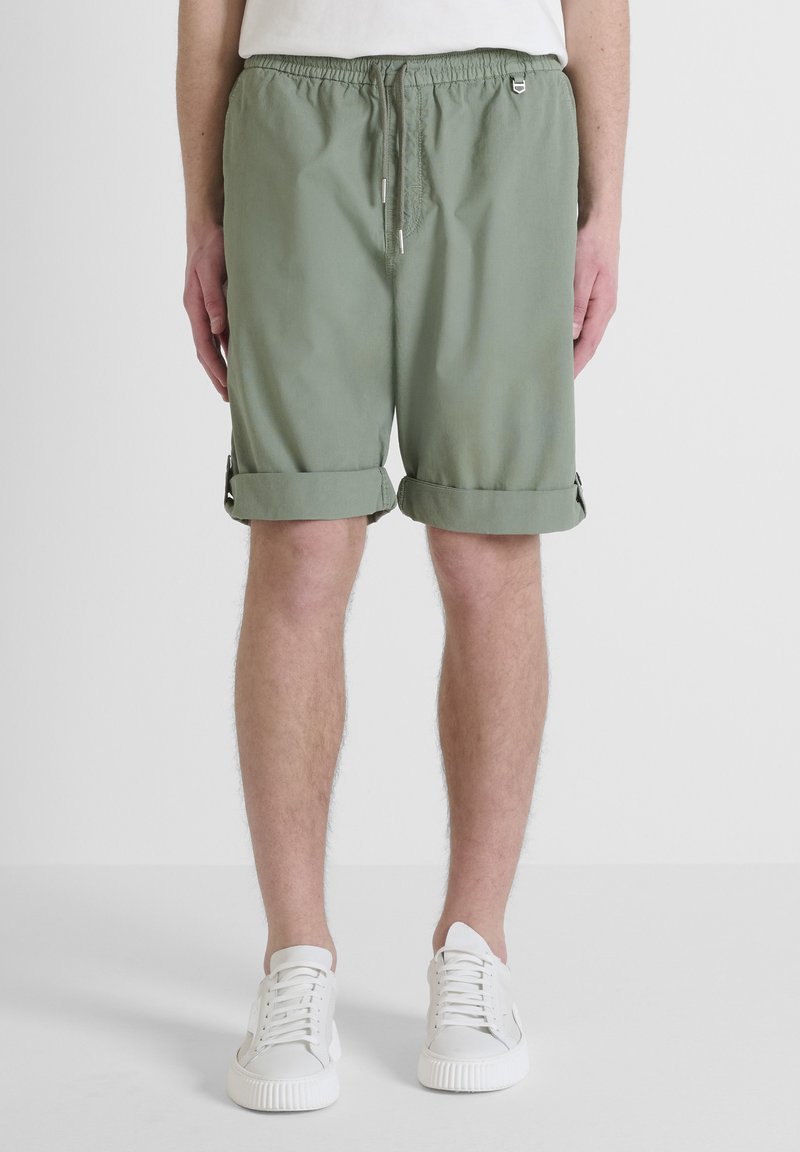 Pantaloni corti verde chiaro realizzati in tessuto morbido, dotati di una vita elasticizzata con coulisse, risvoltini e piccoli dettagli metallici.
