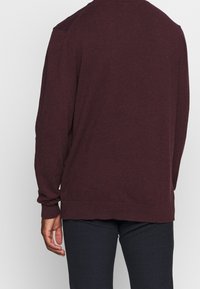 Burgundy stickad tröja med lång ärm, ribbade mudd och nederkant, rundad halsringning, avslappnad passform, mjuk textur och inga synliga mönster eller dekorationer.