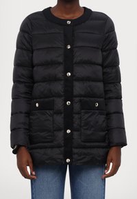 Chaqueta de plumas negra con cuello redondo, cierre de botones a presión, dos bolsillos frontales y acolchado horizontal para el aislamiento.